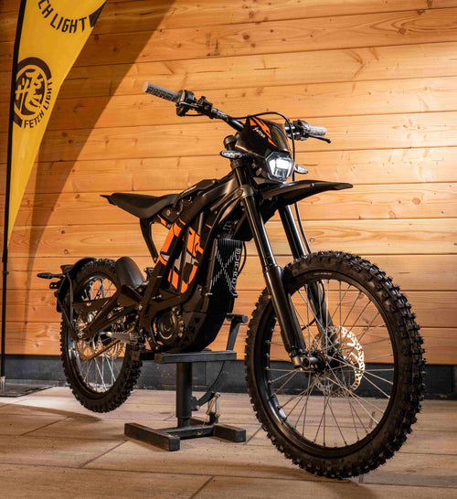 An Surron Light Bee X model parked in front of a rustic wooden wall, showcasing its vibrant color against the natural backdrop